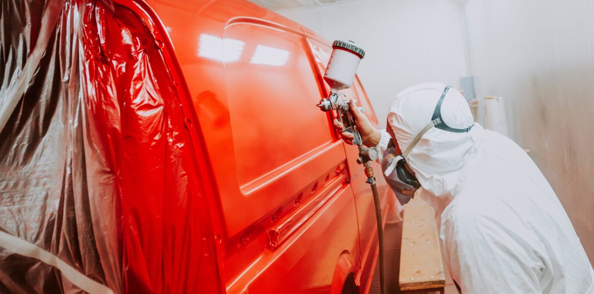 Automotive industry - engineer painting and working on a red bodywork of a car and wearing protective gear