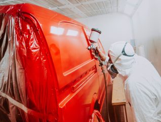 Automotive industry - engineer painting and working on a red bodywork of a car and wearing protective gear